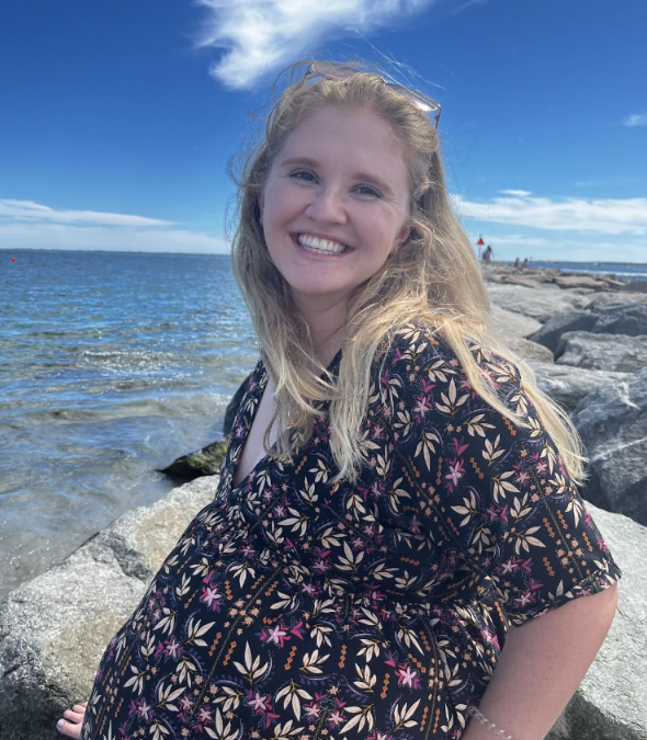 Smiling woman by rocky seaside under blue sky.