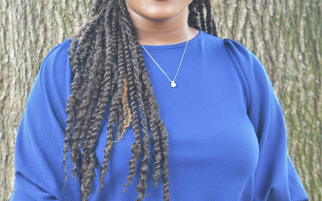 Smiling person in blue shirt, tree background.