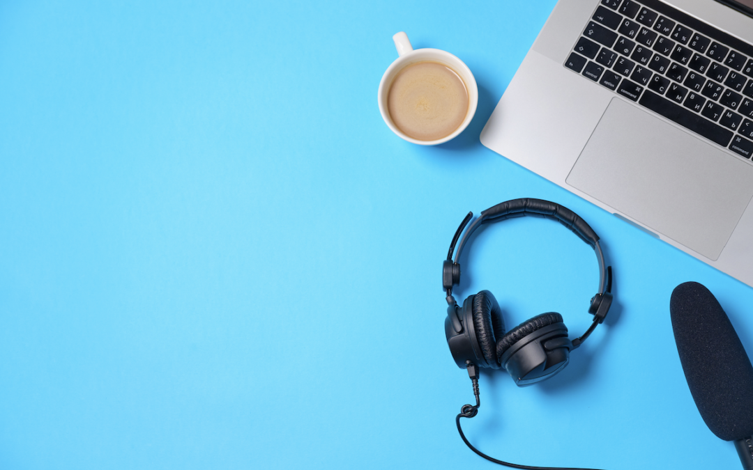 Laptop, headphones, coffee, microphone on blue background.