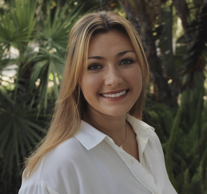 Smiling woman in white shirt, outdoor setting.